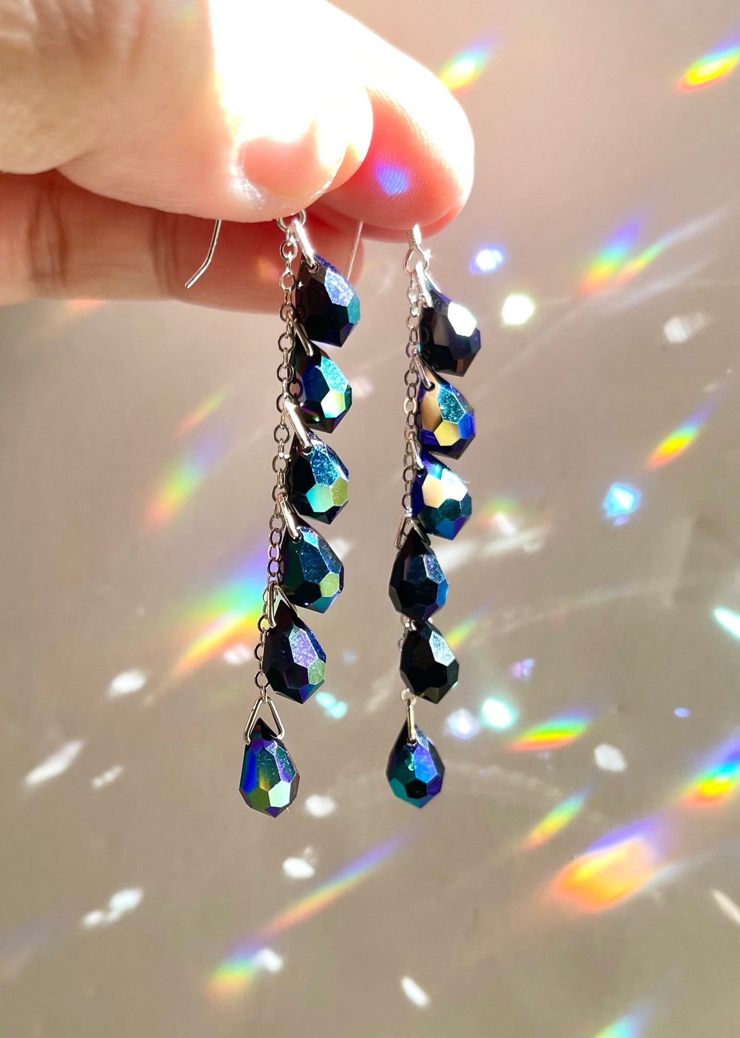 Earrings with black iridescent crystal teardrops hanging in a waterfall cascade